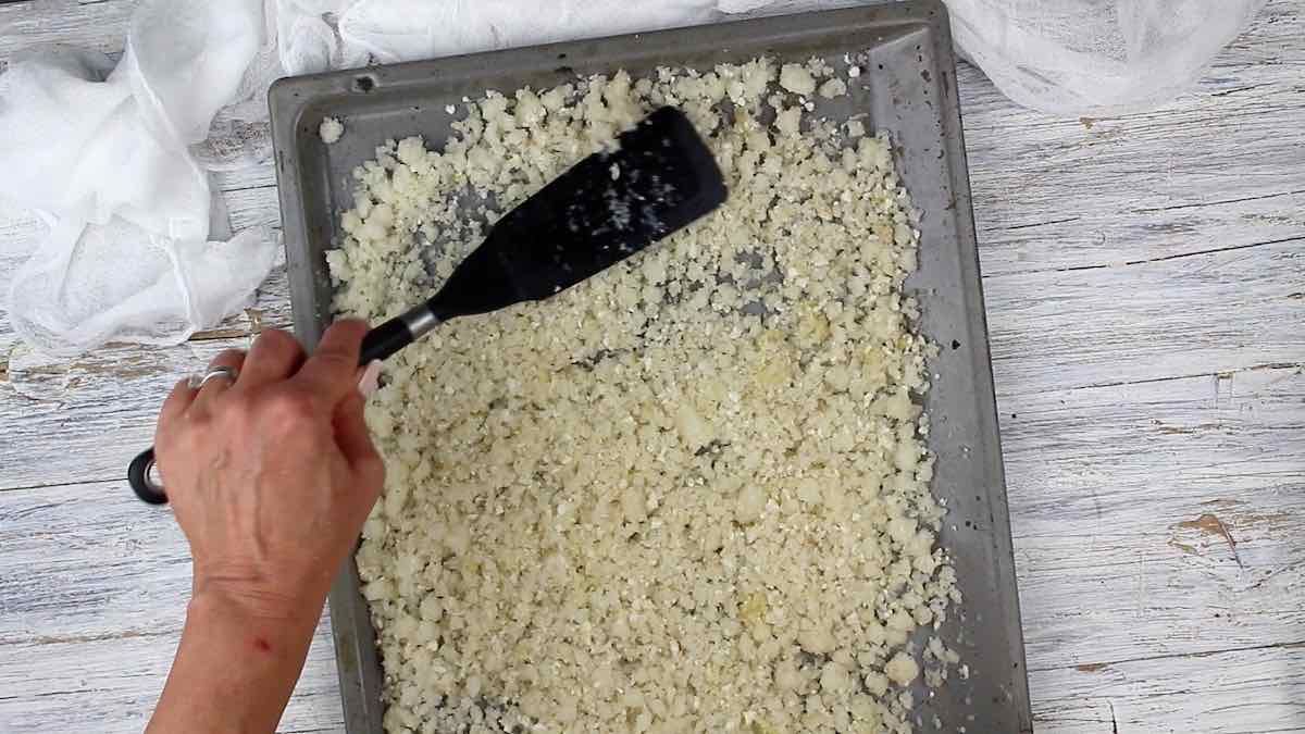 Using a spatula to break frozen cauliflower bits on a baking sheet.