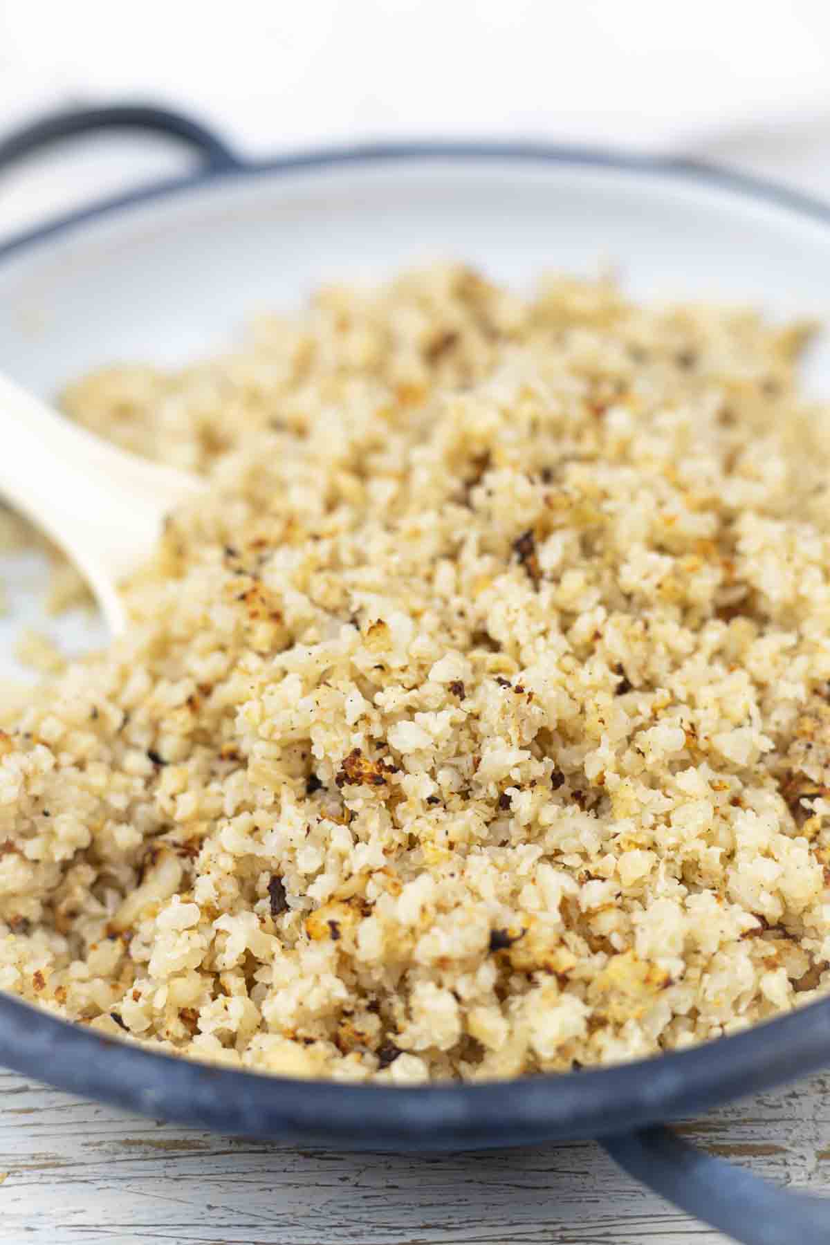 Baked cauliflower in a pan with a wooden spoon.