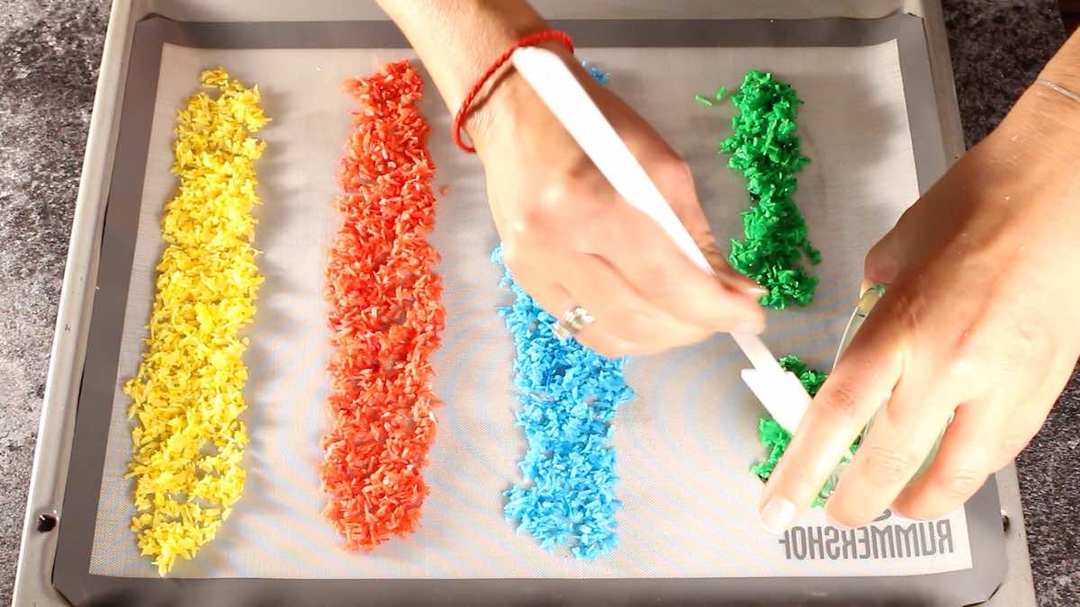 A person is sprinkling colored sprinkles on a baking sheet.