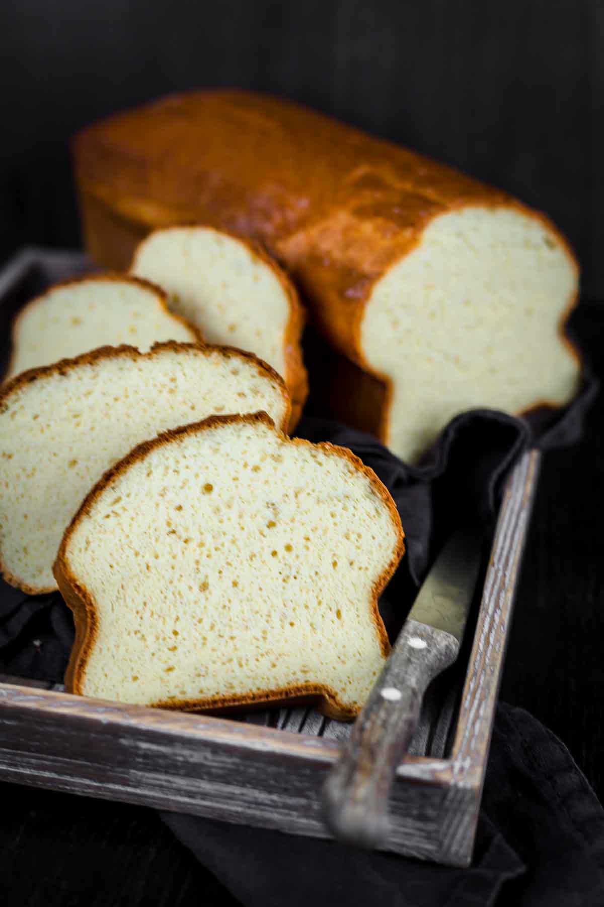 Protein bread slices on a wooden tray with a knife.