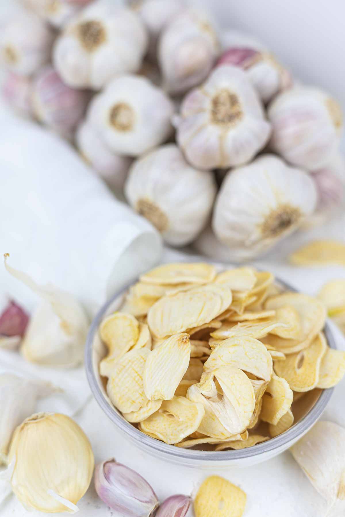 A bowl of garlic chips next to a garlic.