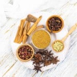 Assorted spices including ground mix, cloves, cardamom, cinnamon sticks, and star anise neatly presented on a wooden surface.