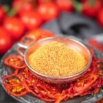 Bowl of tomato powder surrounded by dried tomatoes.