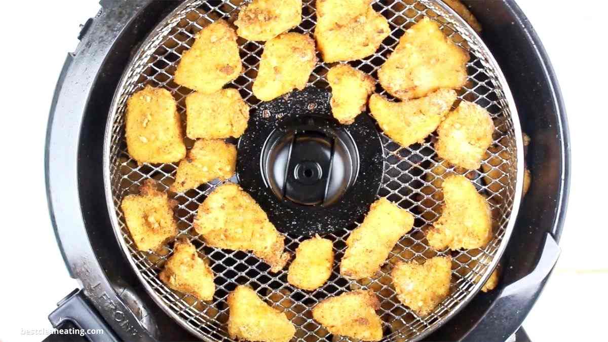 A top view of golden-brown breaded chicken pieces arranged on a round metal mesh tray inside an air fryer.