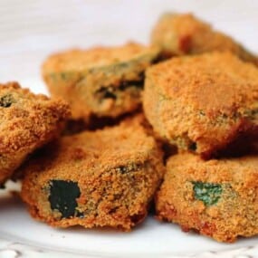 A white plate with several breaded and deep-fried slices of zucchini.