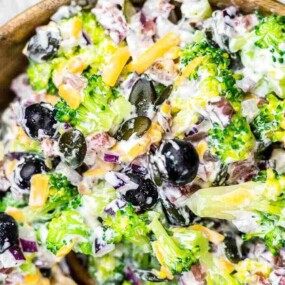 A bowl of broccoli salad with black olives, red onions, shredded cheese, and mayonnaise-based dressing.