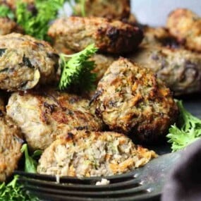 A plate of grilled meat patties garnished with fresh parsley. A fork is also visible, with one patty partially eaten.