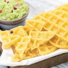Crispy triangular and round cheese crisps are served on a tray with a side of guacamole in a small bowl.