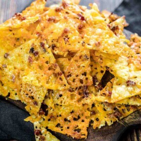 A pile of crispy cheese crackers sprinkled with seasoning, placed on a wooden serving board.