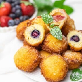 A plate of doughnuts filled with berries and dusted with powdered sugar, garnished with mint leaves. A small bowl of strawberries and blueberries in the background.