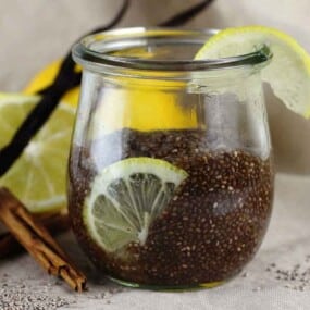 A jar filled with chia seed pudding, garnished with a lemon slice, sits on a beige cloth next to lemon slices and cinnamon sticks.