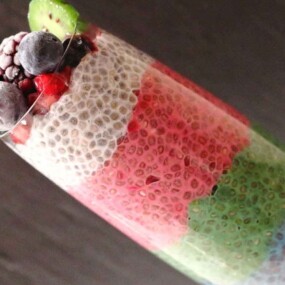 A layered chia seed pudding in a clear glass with colorful, distinct layers, topped with frozen berries and a slice of kiwi.