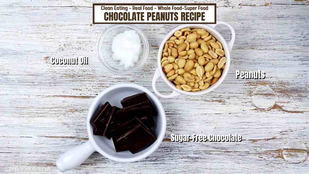 Ingredients for chocolate peanuts recipe displayed on wooden surface, featuring bowls of coconut oil, sugar-free chocolate, and peanuts, labeled clearly.