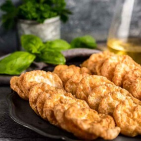 A plate of golden brown cloud bread is placed on a dark surface, with fresh herbs and a glass container of oil in the background.