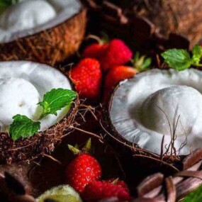 Halved coconuts filled with white ice cream, garnished with mint leaves, surrounded by strawberries.