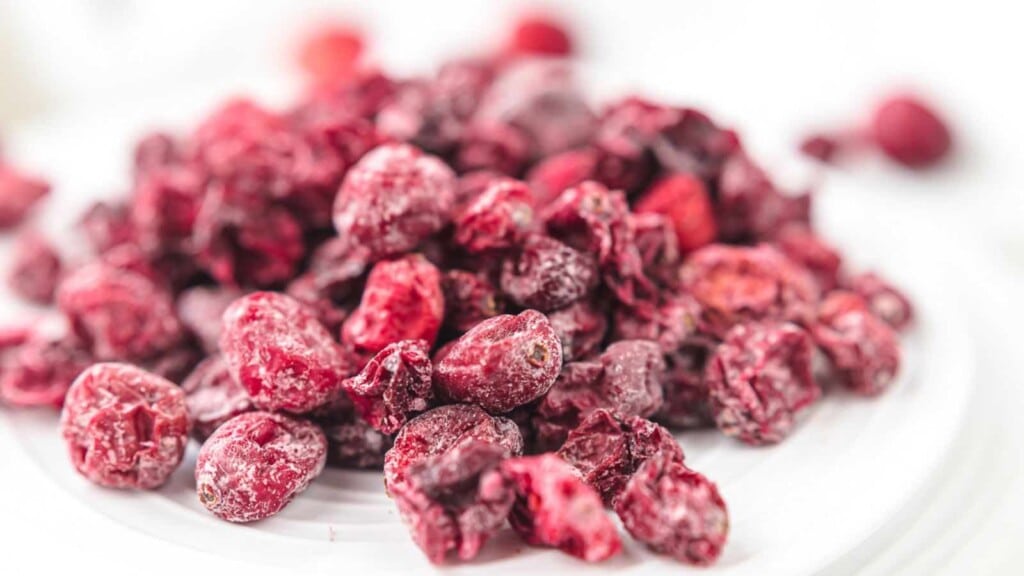 Close-up image of a pile of dried red cranberries on a white surface.
