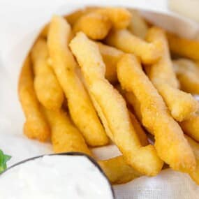 A plate of freshly made churros with a side of dipping sauce.