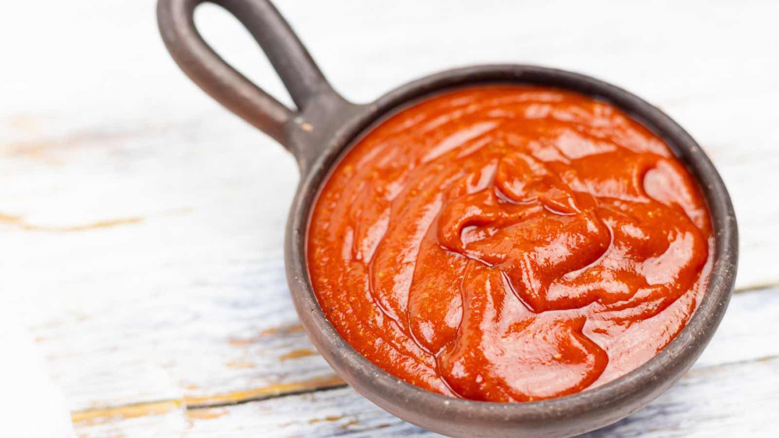 A black bowl filled with smooth, red tomato sauce sits on a light-colored wooden surface.