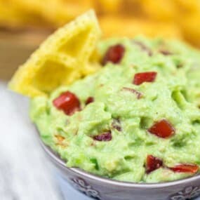 A bowl filled with guacamole garnished with diced tomatoes and a tortilla chip.