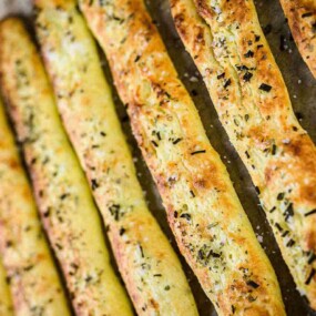 Freshly baked breadsticks seasoned with herbs and displayed in a row on a parchment-lined baking sheet.