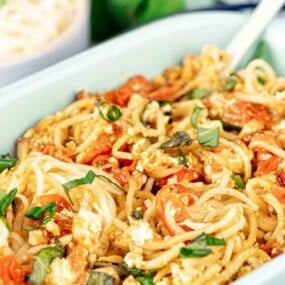A dish of baked feta pasta with spaghetti, cherry tomatoes, and basil in a white baking dish.