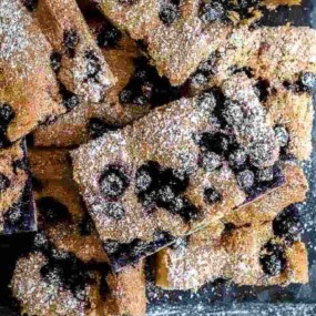 A stack of rectangular, sugar-dusted baked goods with visible blueberries on a dark surface.
