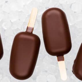 Four chocolate-coated ice cream bars on wooden sticks are arranged on a bed of ice crystals.