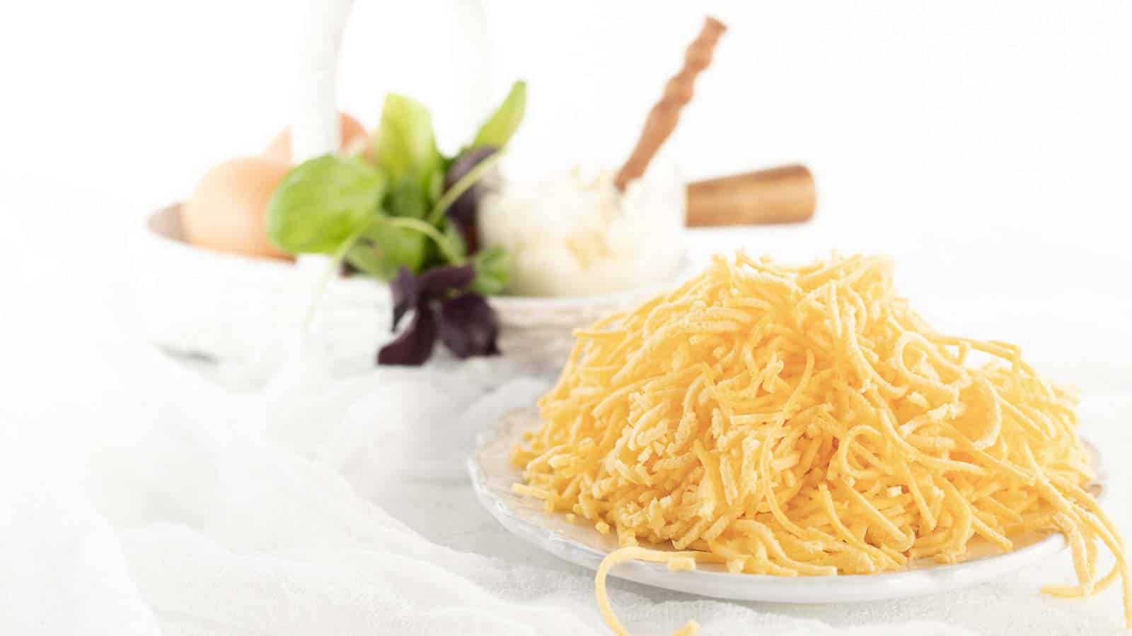 A plate of grated cheese is in front. In the background, there is a small white basket with eggs, greens, and a wooden-handled utensil.