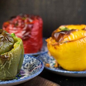Three cooked stuffed bell peppers in green, red, and yellow sit on blue and white patterned plates.