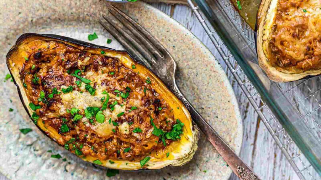 A baked stuffed eggplant topped with melted cheese and garnished with chopped herbs, placed on a plate with a fork beside it.