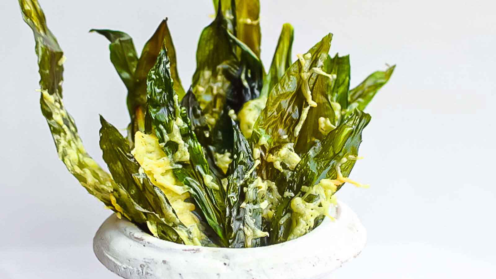 A white bowl filled with green leafy vegetables coated in a yellow sauce.