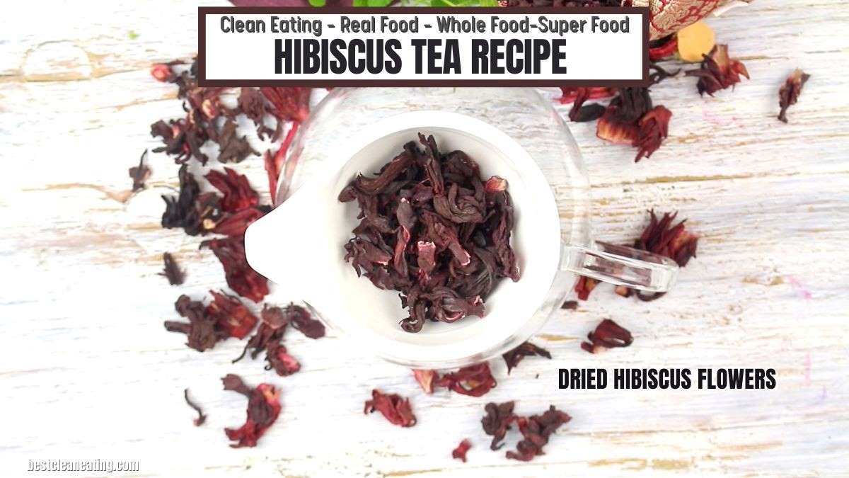 A white cup filled with dried hibiscus flowers, surrounded by scattered hibiscus petals, with a recipe title and description at the top of the image. Text at the bottom right reads "DRIED HIBISCUS FLOWERS.