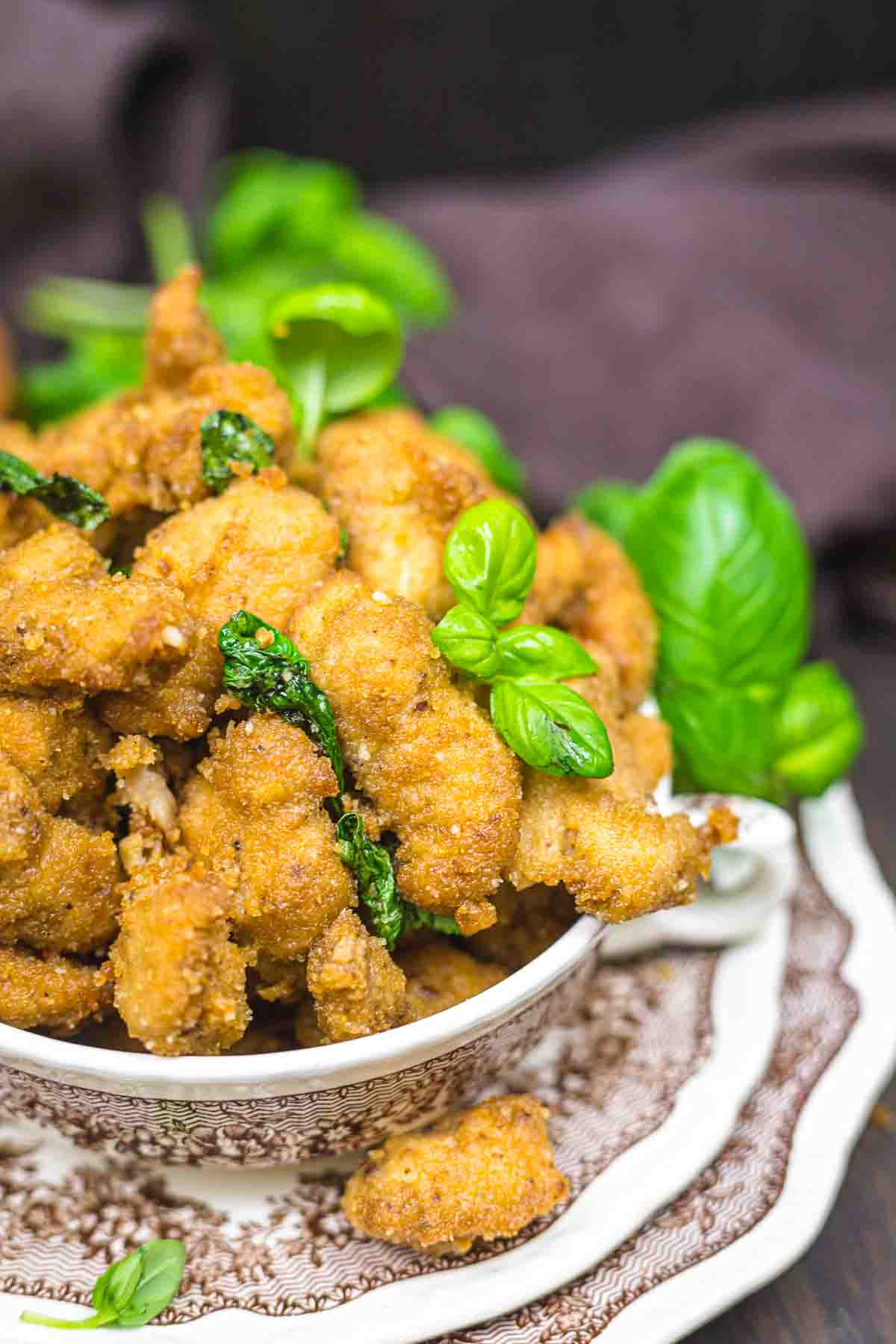 A plate filled with crispy, golden-brown fried chicken garnished with fresh green basil leaves, served on a patterned ceramic dish.