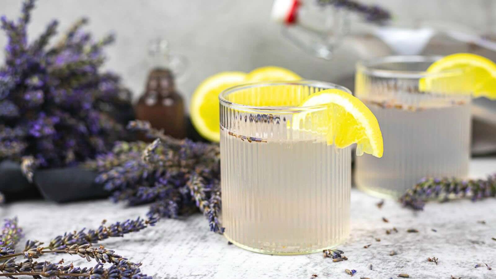 Two glasses of lavender lemonade are garnished with lemon slices.