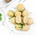 A plate of dumpling balls garnished with chopped parsley, with one matzo ball cut in half to show the interior texture.