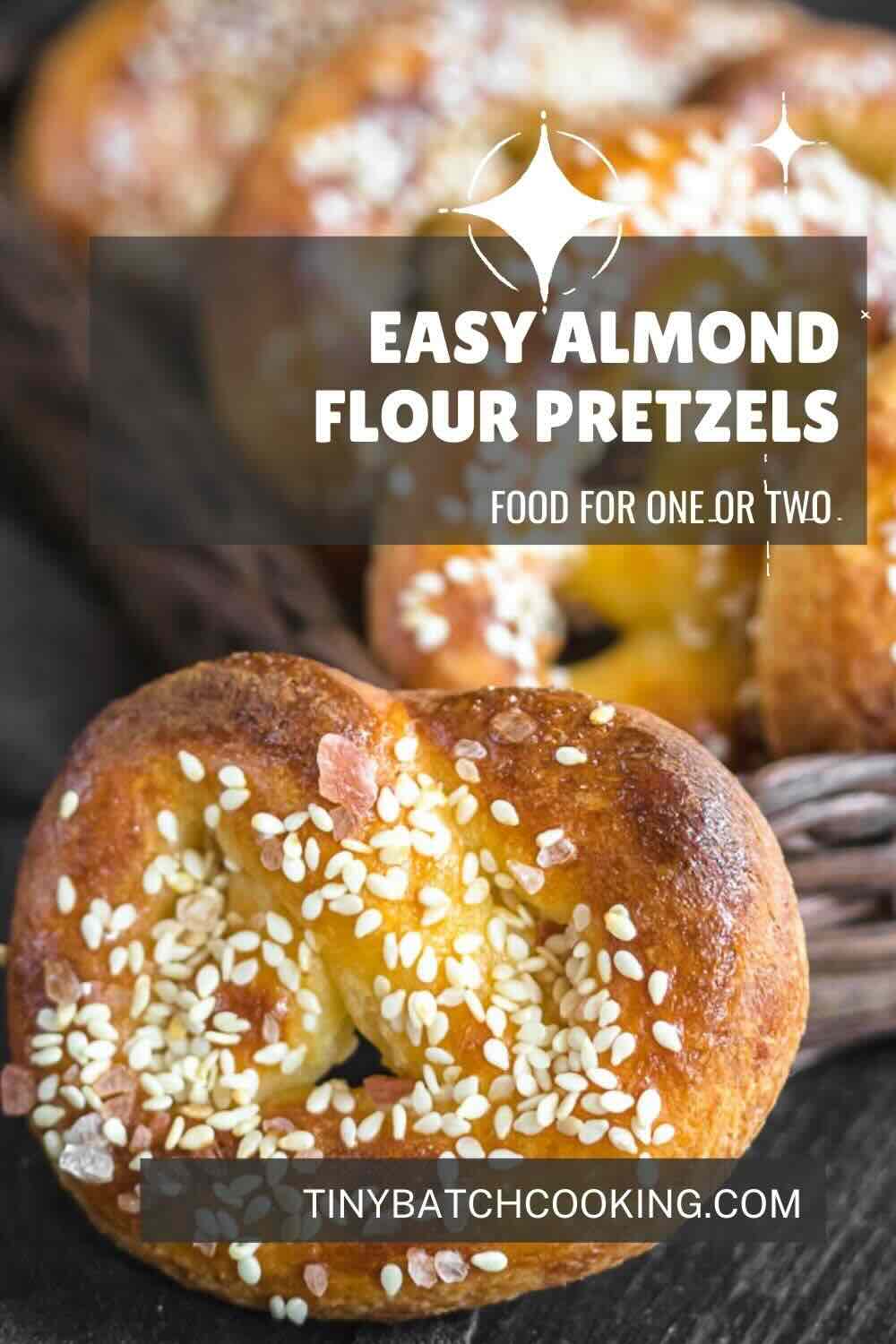 Close-up of freshly baked pretzels made with almond flour, topped with sesame seeds and salt, with an overlaid text promoting the recipe for one or two on a website, tinybatchcooking.com.