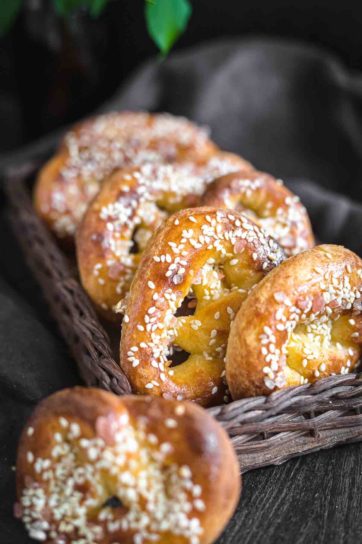 A close-up shot of a basket filled with pretzels coated with sesame seeds, placed on a dark cloth background.