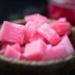 Close-up of bright pink diced pickled radishes in a wooden bowl against a dark background.