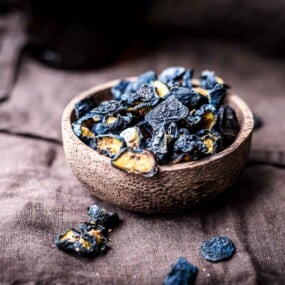 A bowl filled with dark blue dried blueberries.