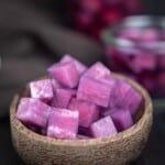A bowl filled with purple blueberry pickled radishes with a blurred background showing more cubes in a glass container.