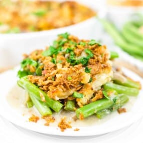 A plate of green bean casserole topped with crispy onions and fresh parsley, with a creamy white sauce underneath.