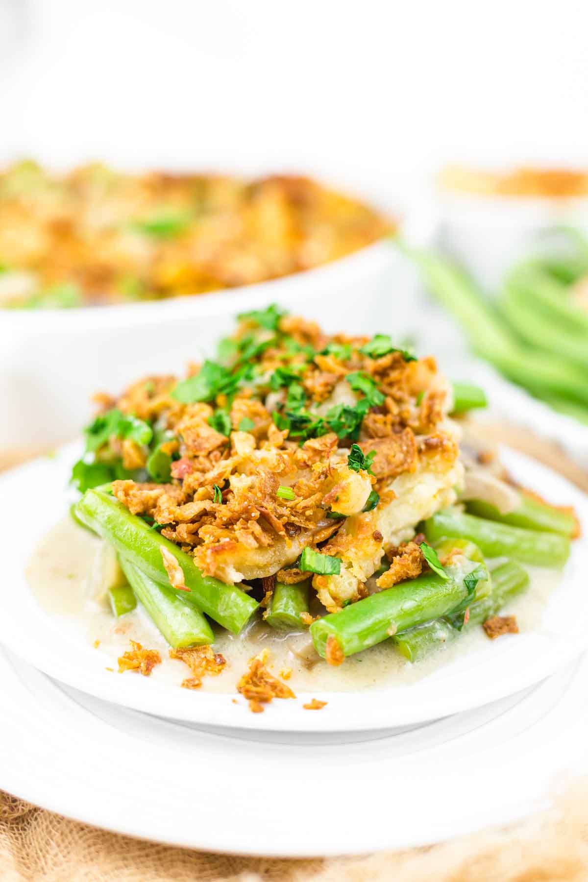 A plate of green bean mushroom casserole topped with crispy fried onions and garnished with herbs is shown.