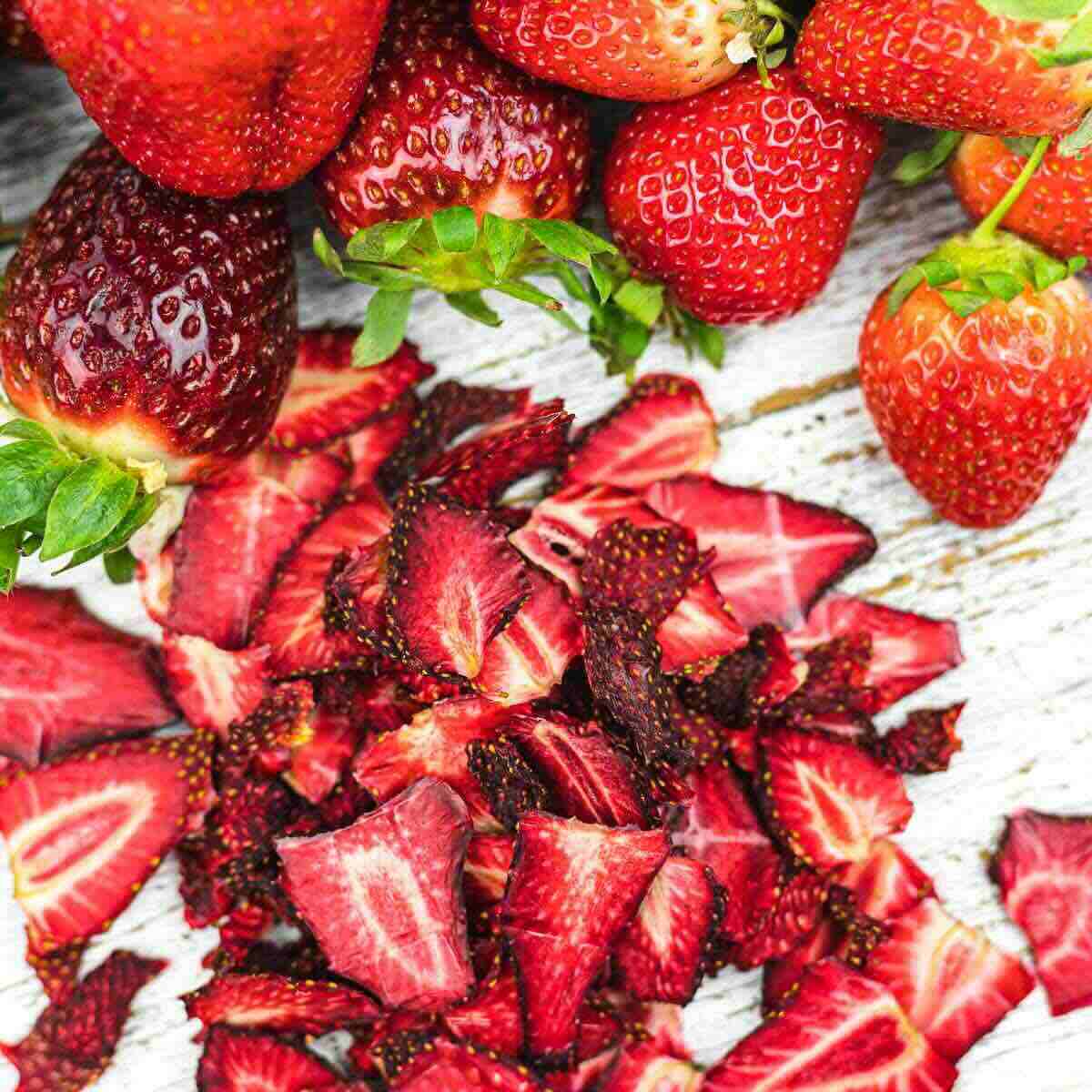 Whole strawberries and diced strawberry pieces on a white wooden surface.