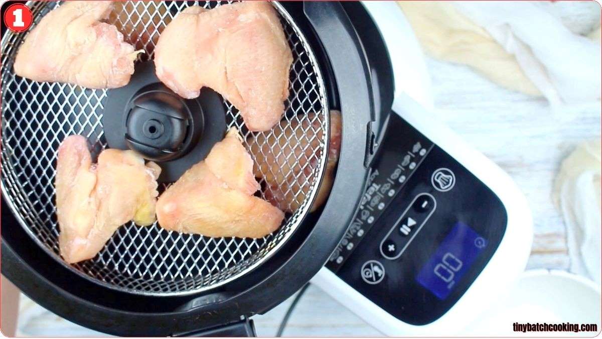 Top view of raw chicken wings arranged on an air fryer tray next to a digital control panel displaying “0” at the start of cooking.