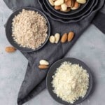 Two plates with ground almonds and almond flours, including almonds, arranged on a gray cloth napkin on a light gray countertop.