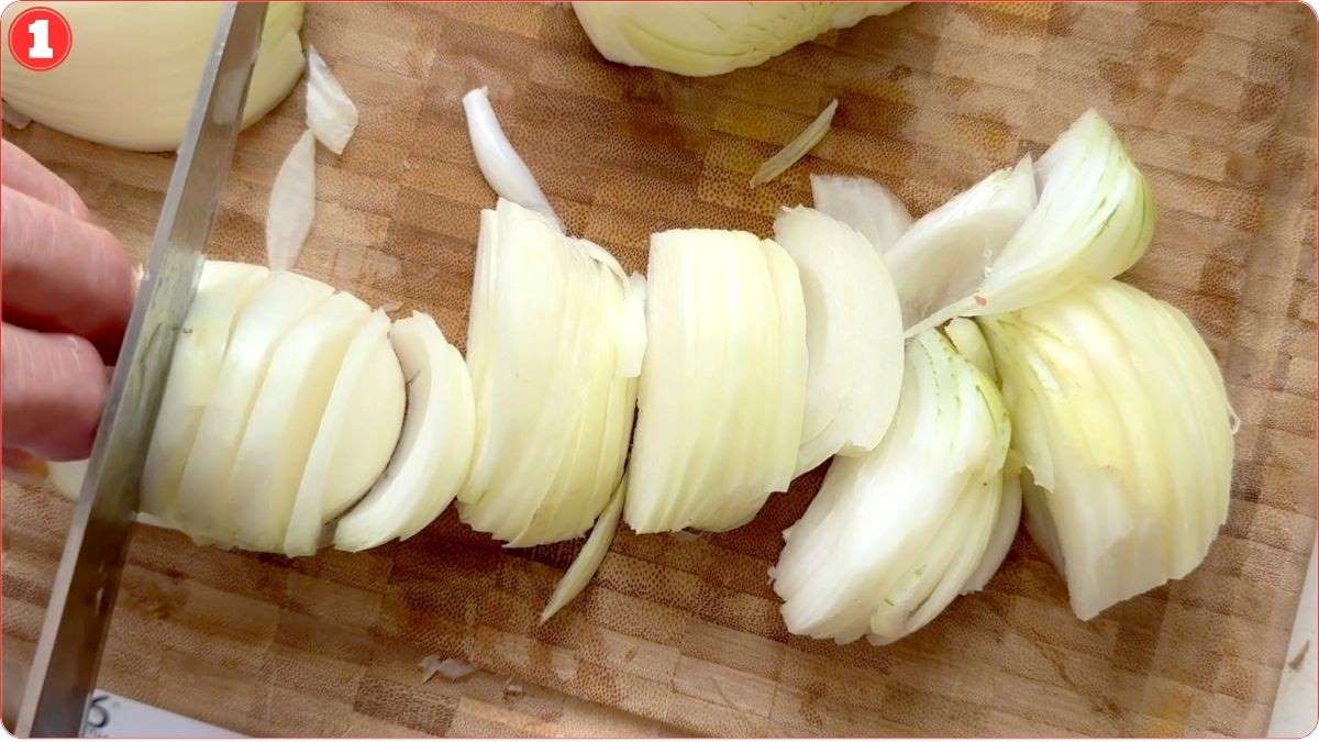 A close-up of a hand slicing an onion with a knife on a wooden cutting board. Several onion slices are visible.