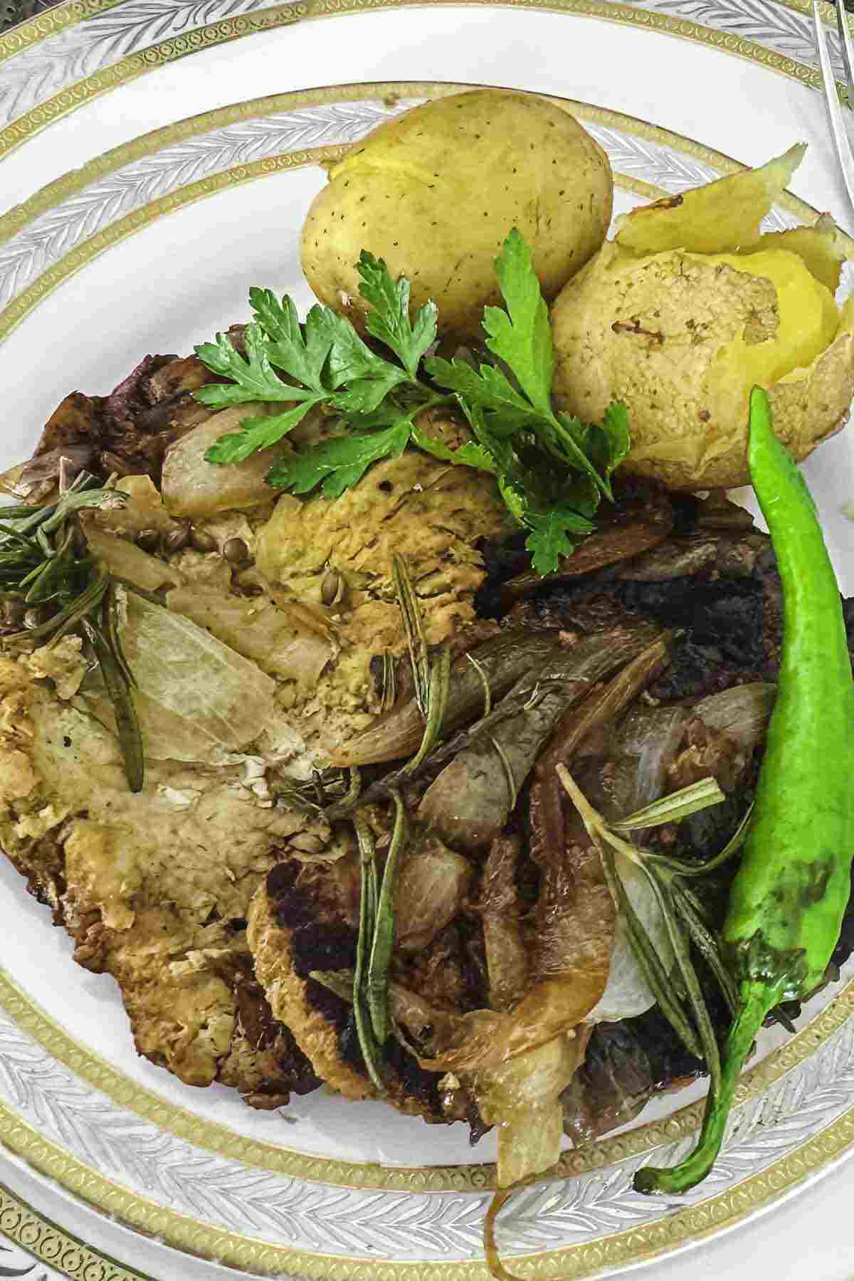 A plate of pork fillet meat garnished with parsley and a green chili pepper, served with roasted potatoes and caramelized onions.