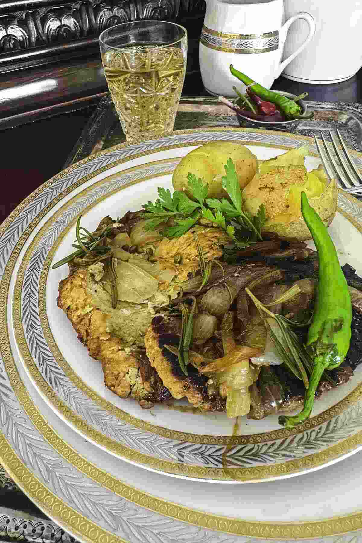 A plate of A plate of pork fillet dish garnished with herbs. A glass of beverage and a white jug are in the background.