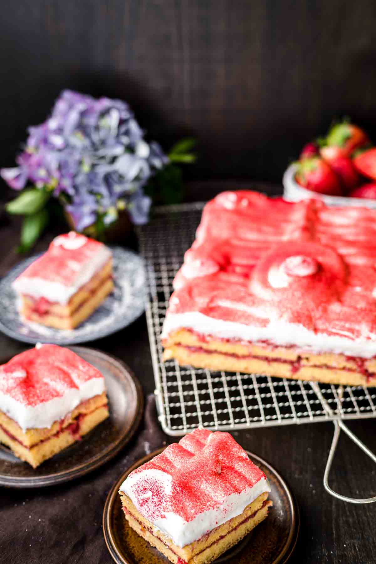 Slices of strawberry sheet cake with a white icing and topped with strawberry powder.
