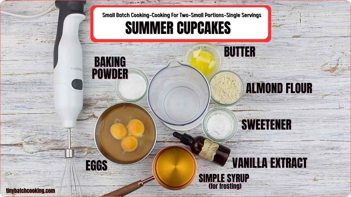 Image shows ingredients and equipment for making summer cupcakes, including eggs, baking powder, almond flour, butter, sweetener, vanilla extract, and simple syrup, arranged on a wooden surface with a hand mixer.